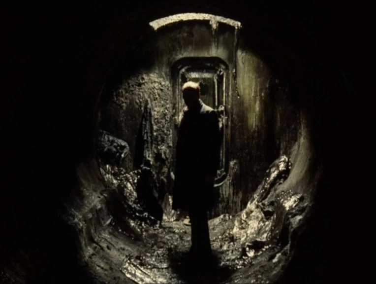 Stalker (1979) movie still: medium — A damp and filthy industrial pipe features slick, textured walls covered in dark slime. A lone man in a trench…