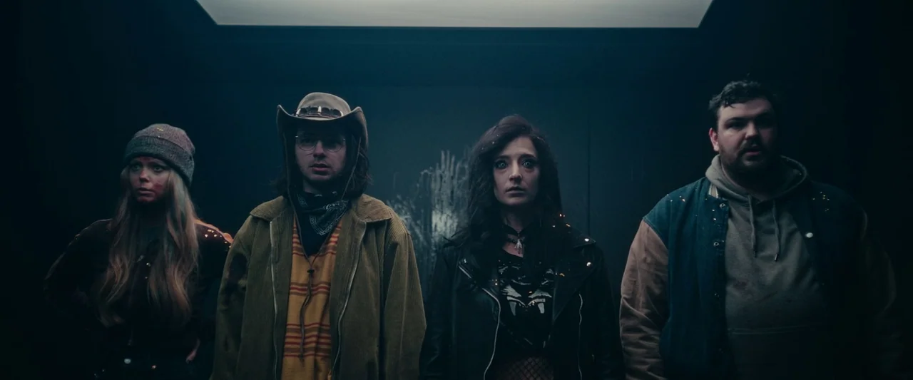 We Are Zombies (2023) movie still: medium — Four individuals stand in a dimly lit, narrow metal space with dark walls. They are aligned horizontally…
