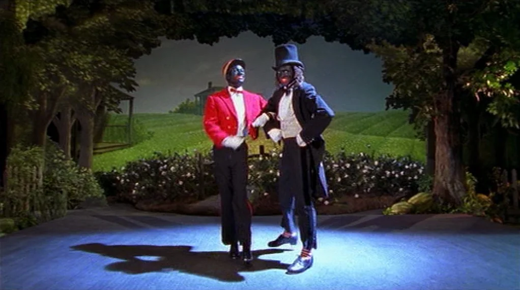 Bamboozled (2000) movie still: fullbody — A theatrical stage set features a painted rural landscape backdrop behind two performers. Two men in…