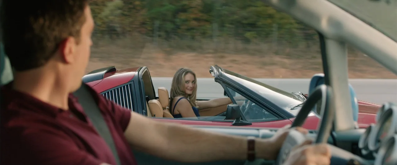 Vacation (2015) movie still: medium — A woman in a red convertible drives alongside a man on a paved highway. The woman looks over at the man while…