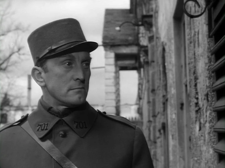 Paths of Glory (1957) movie still: medium — An outdoor area near a stone wall structure with vintage architectural features. A man in a military…