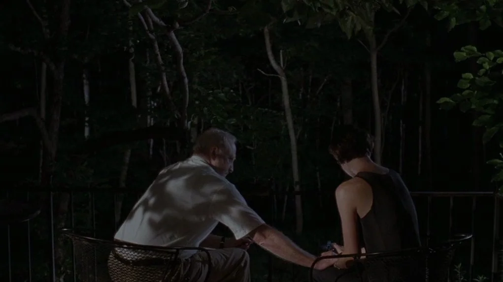 Junebug (2005) movie still: medium — An older man and a young woman sit together on a metal bench at night. They are positioned outdoors in front of…