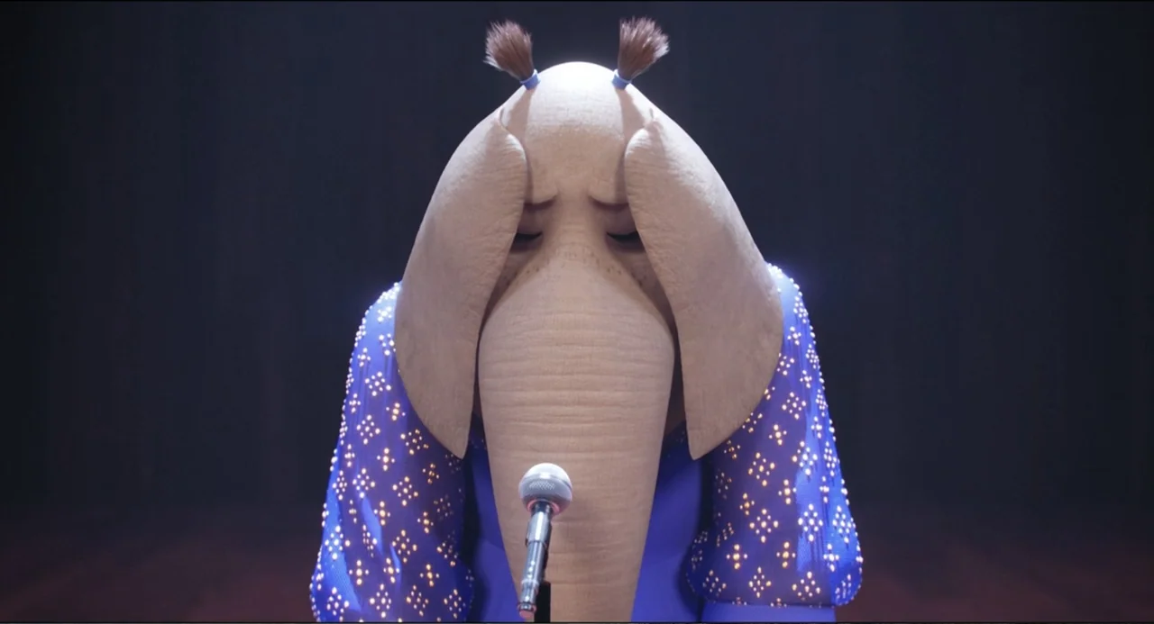 Sing (2016) movie still: medium — A dark stage features an anthropomorphic elephant performing under a single focused spotlight. The subject stands…