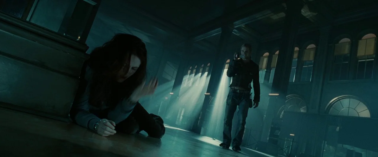 Twilight (2008) movie still: wide — A spacious dark hall with tall windows emits light into the interior space. A woman lies on the floor while a…