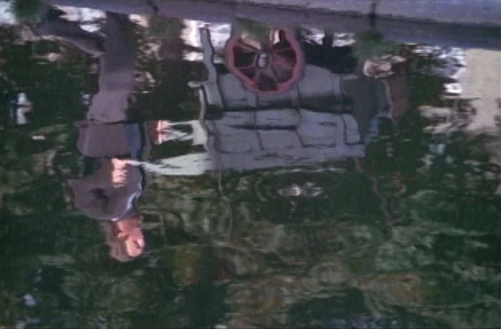 Quackser Fortune Has a Cousin in the Bronx (1970) movie still: medium — A murky puddle on the ground reflects the image of a man in a suit. The…