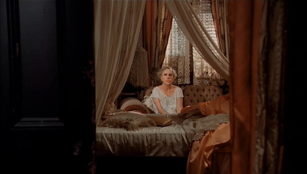 Pretty Baby (1978) movie still: medium — An ornate bedroom features a draped canopy bed with lace curtains and layered fabrics. An elderly woman…