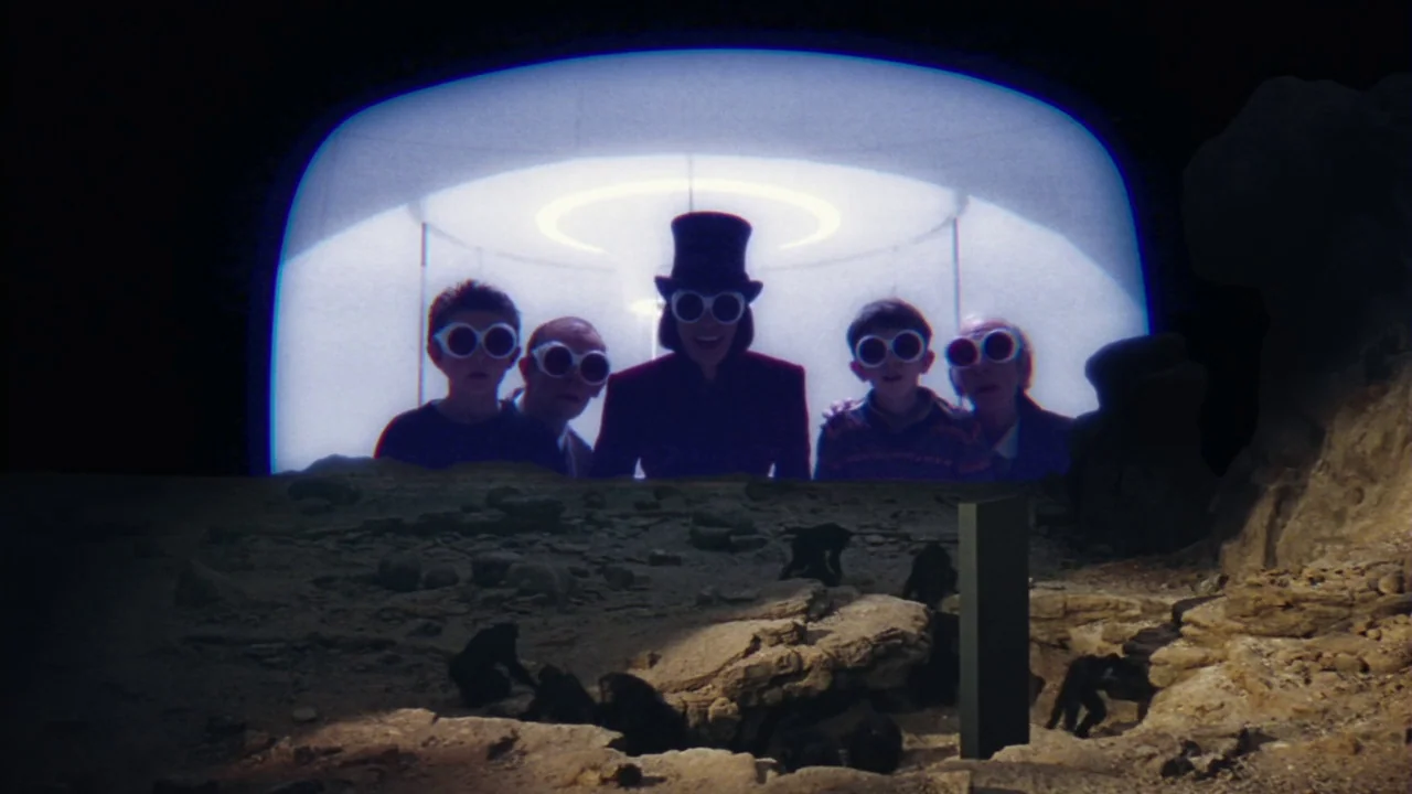 Charlie and The Chocolate Factory (2005) movie still: wide — Five people wearing white-rimmed sunglasses watch a projection of prehistoric apes on a…
