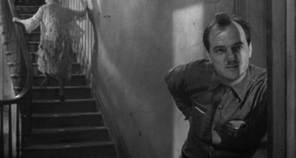 Baby Doll (1956) movie still: medium — An interior stairwell features wooden steps and a simple railing against a plain wall. A man in the…