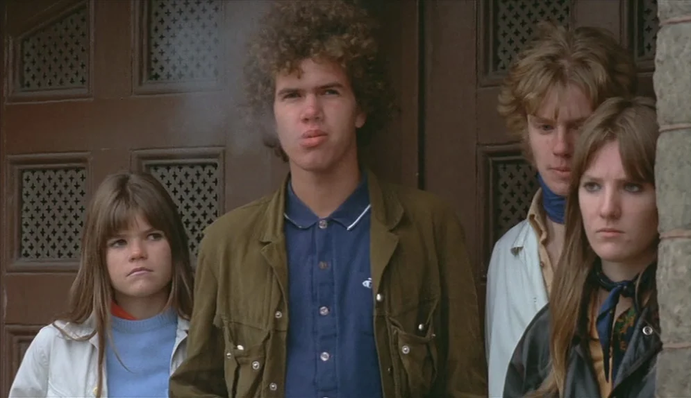 A Swedish Love Story (1970) movie still: medium — A group of four teenagers stands before a set of dark brown wooden doors. The individuals remain…