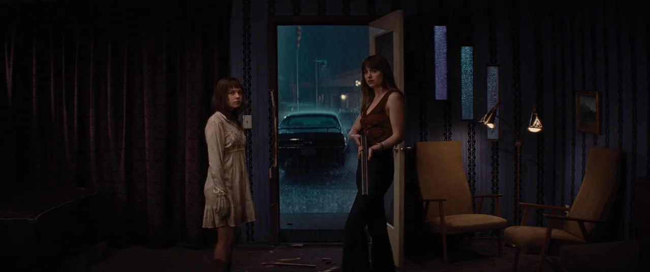 Bad Times at the El Royale (2018) movie still: wide — A dark motel room with blue wallpaper and vintage furniture opens into a rainy parking lot.…