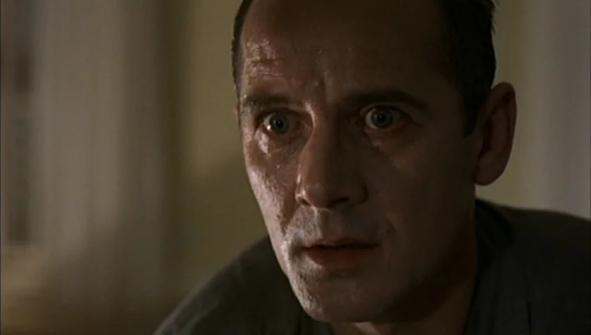 Funny Games (1997) movie still: closeup — A dimly lit room provides a blurred background for a close-up portrait shot. A middle-aged man with wide…
