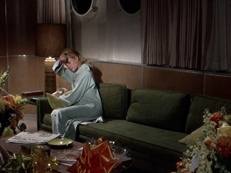 Marnie (1964) movie still: medium — A cabin interior features a green sofa against a wood-paneled wall with portholes. A woman wearing a blue robe…
