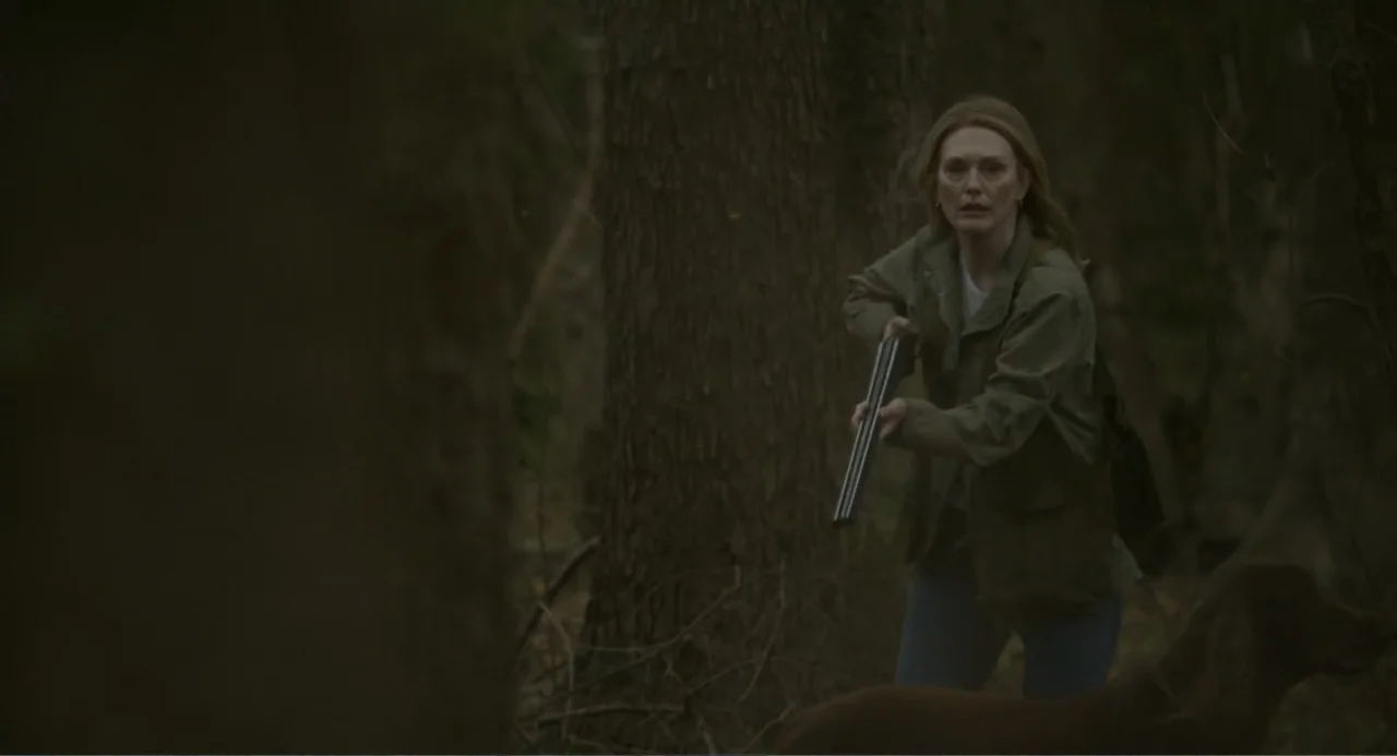 May December (2023) movie still: medium — A dense patch of woodland with large tree trunks framing the composition. A woman stands among the trees…