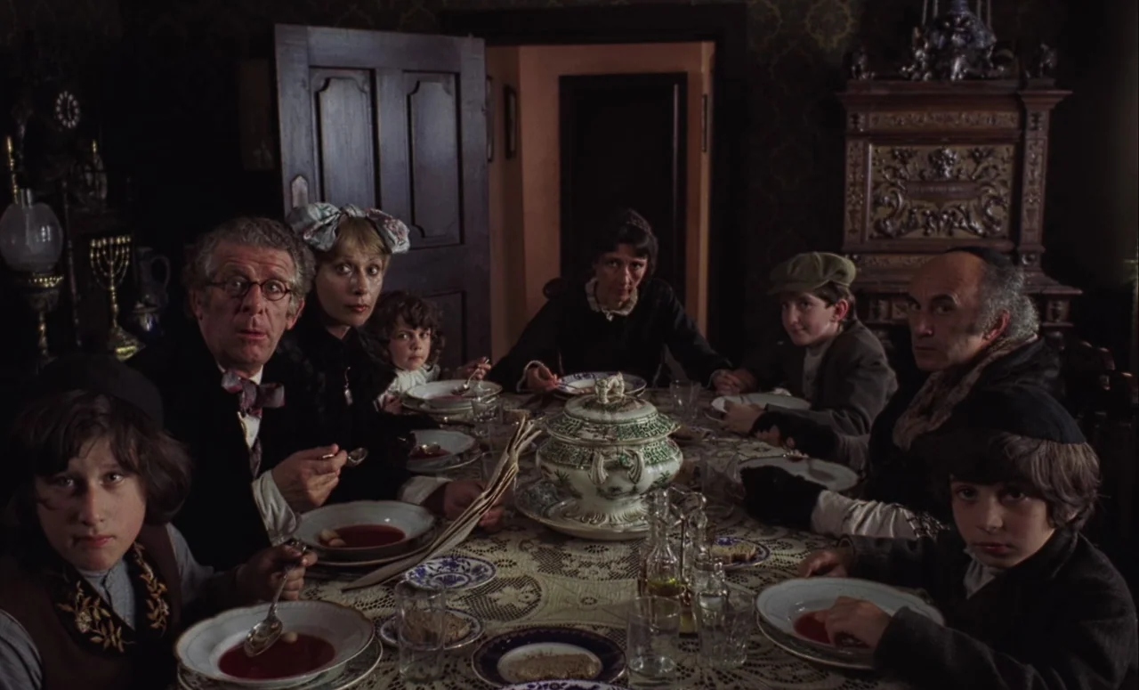 Mahler (1974) movie still: medium — A family sits around a long wooden table covered with a lace tablecloth. The group is eating from bowls at a…