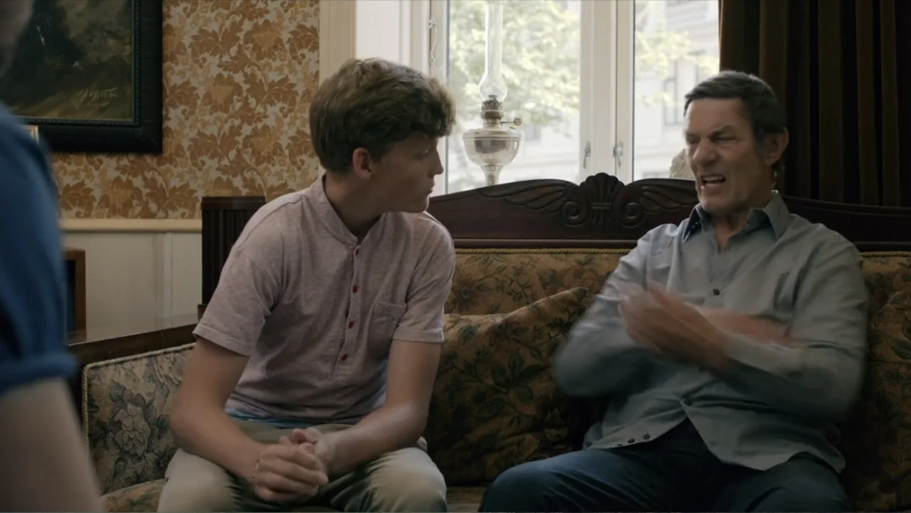 Copenhagen (2002) movie still: medium — A domestic living room features patterned wallpaper and an antique sofa near a window. A teenage boy sits…