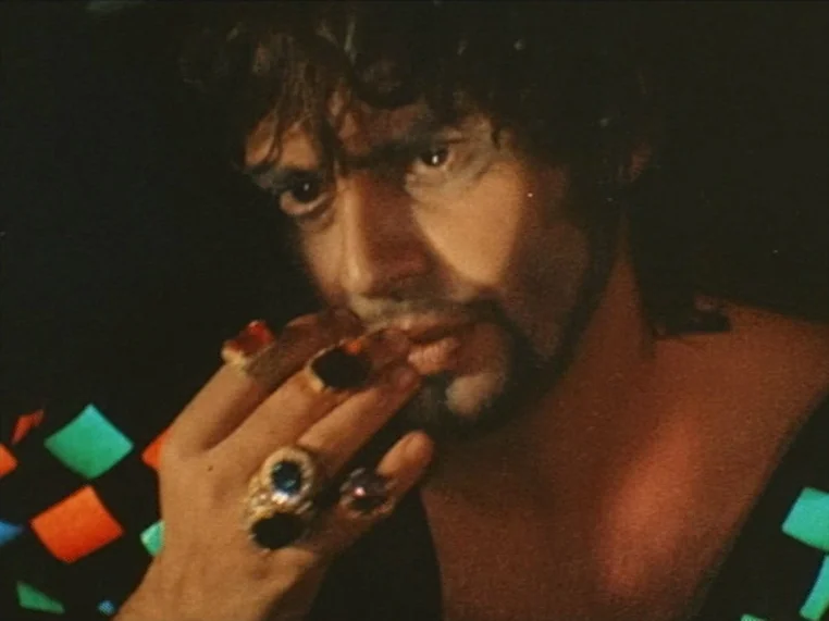 Salome (1972) movie still: closeup — A dark space with a man wearing several large rings on his fingers. He holds his hand near his mouth with a…