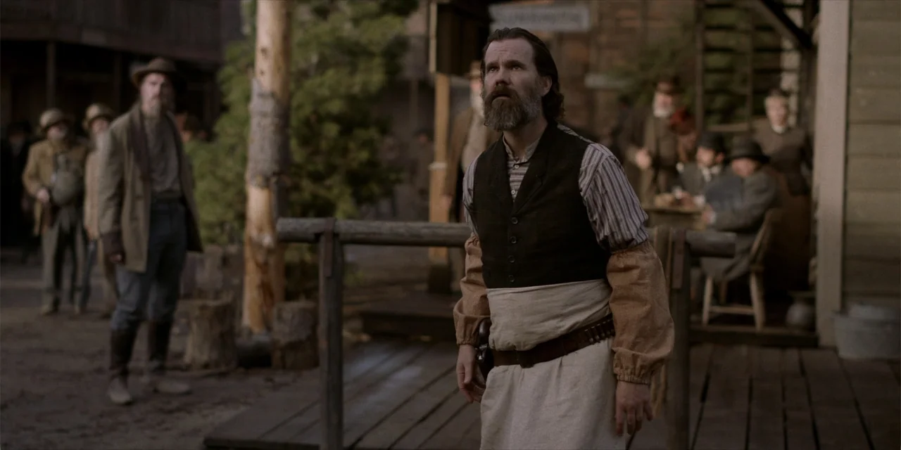 Deadwood: The Movie (2019) movie still: medium — A dusty 1800s western town features wooden storefronts and a crowded dirt street area. A bearded…