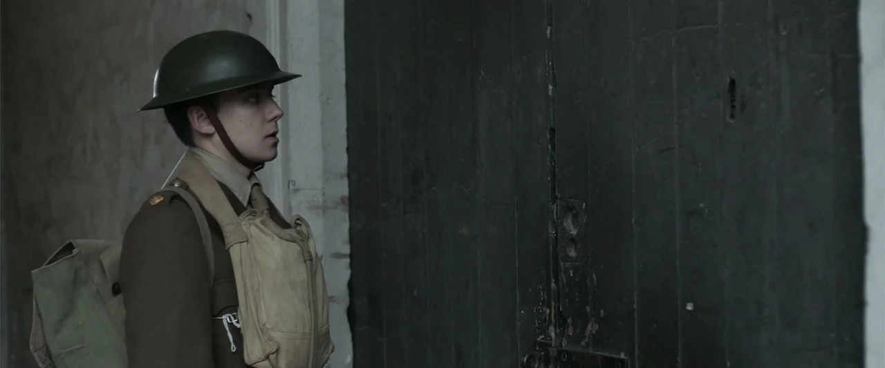 Gone Missing -  Old John's Final Journey (2014) movie still: medium — A soldier in uniform stands in a sparse, neutral-walled corridor. He faces a…