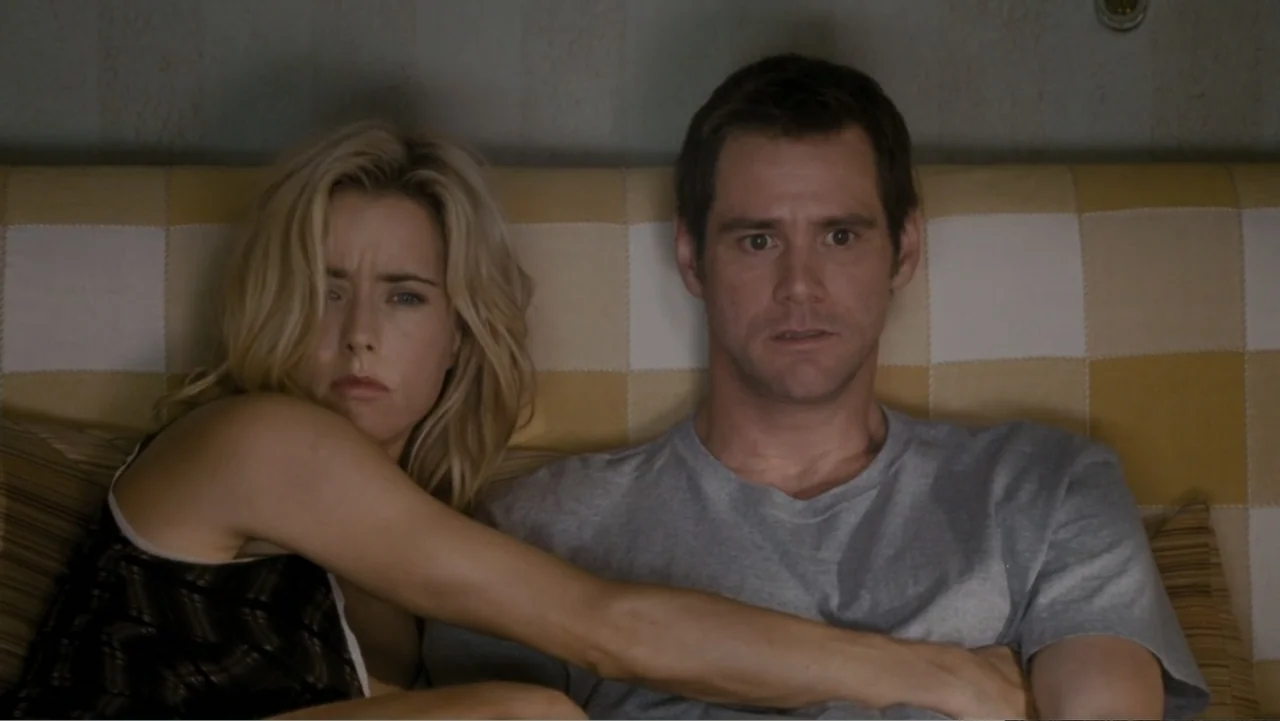 Fun with Dick and Jane (2005) movie still: medium — A room with a yellow and white checkered headboard against a plain wall. A man and a woman sit…