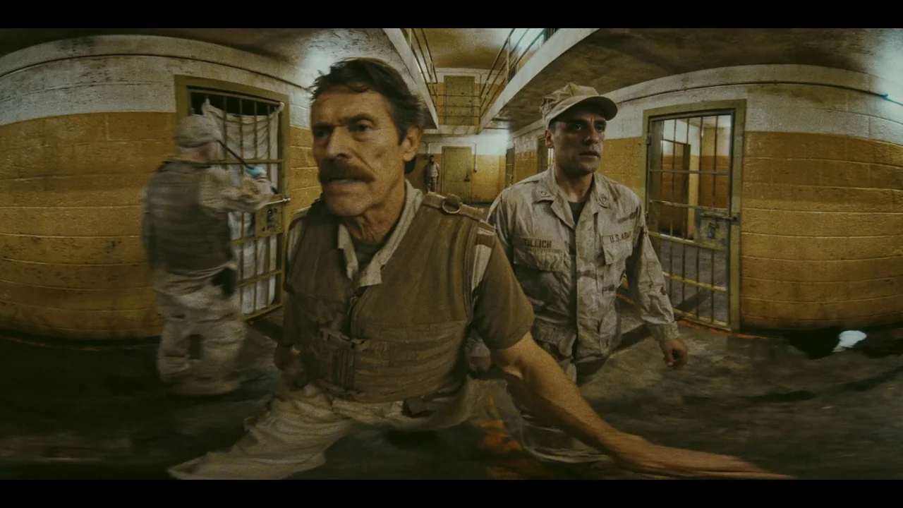 The Card Counter (2021) movie still: medium — A derelict military prison block with concrete walls and multiple iron-barred cells. Two men in desert…