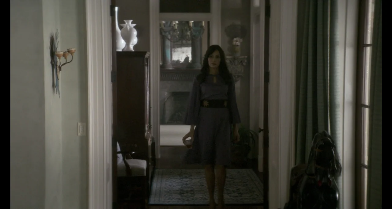 The Poison Rose (2019) movie still: fullbody — A residential hallway features white door frames and a patterned rug on the floor. A woman in a…