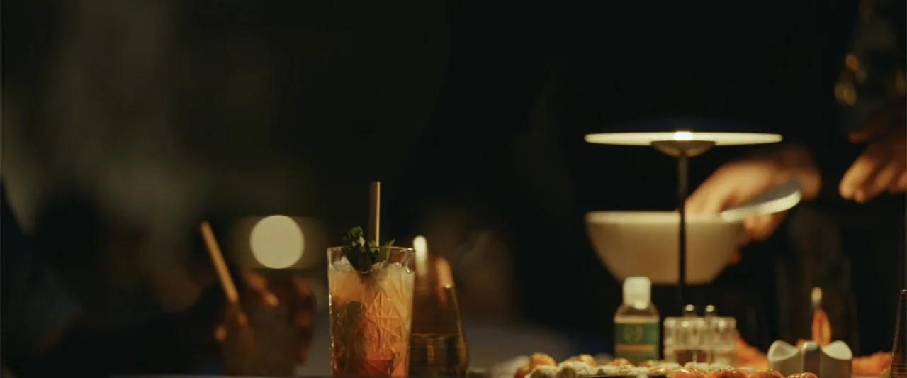 Giannis: The Marvelous Journey (2024) movie still: medium — A low-lit restaurant table features a cocktail glass with a straw and small plates. A…