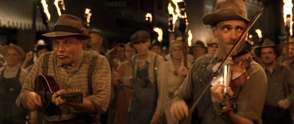 O Brother, Where Art Thou? (2000) movie still: medium — A nighttime gathering occurs outdoors with men holding flaming torches to illuminate the…