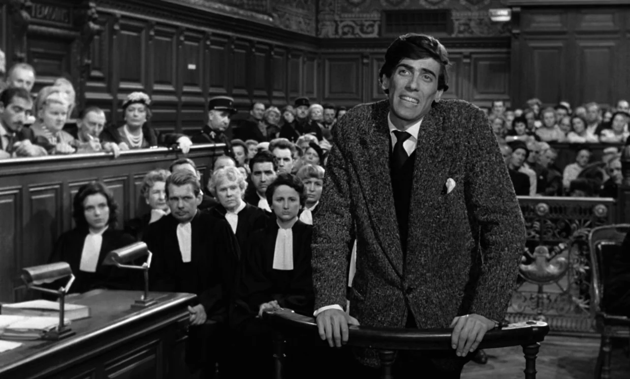 La Verite (1960) movie still: medium — A dark wood-paneled courtroom is filled with legal professionals and observers in the background. A young man…