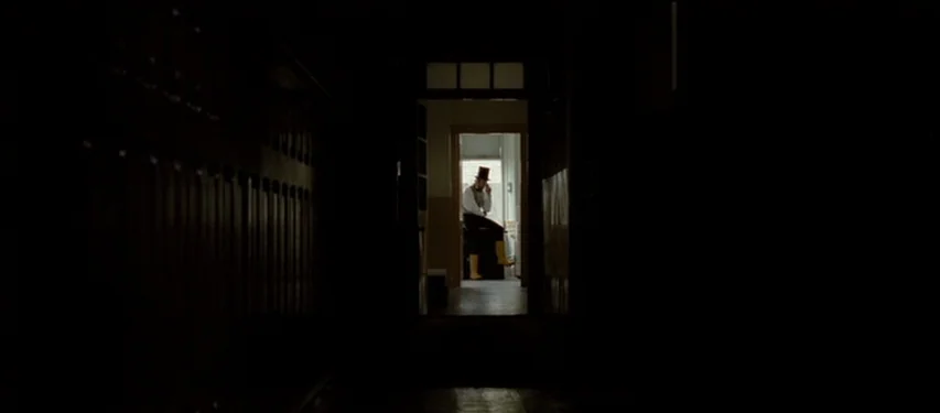 Mister Lonely (2007) movie still: wide — A dark, long interior hallway leads toward a bright room illuminated by natural window light. A man in a…