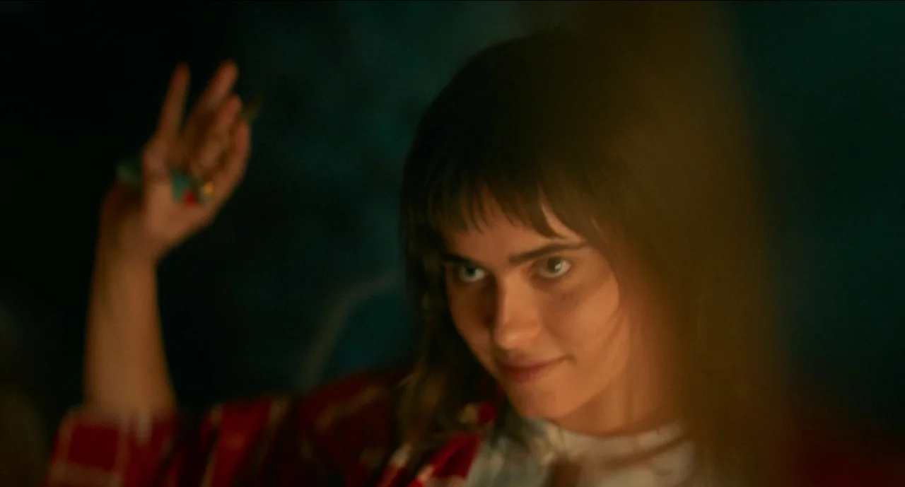Trim Season (2023) movie still: closeup — A dark interior setting shows a person in a plaid shirt. The subject holds their hand up with rings while…