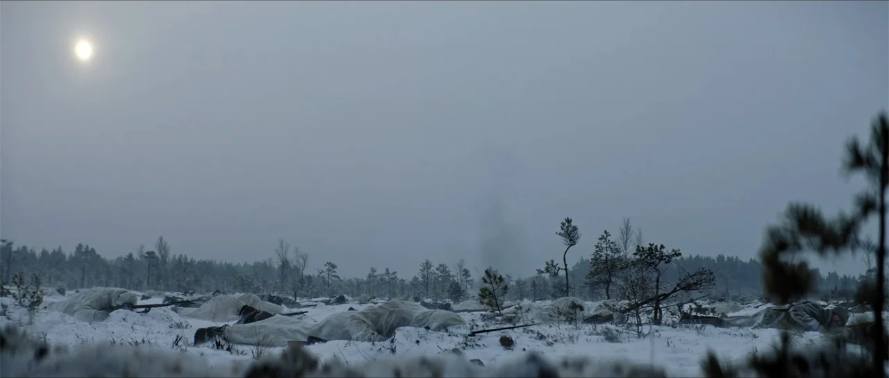 The Rifleman (2019) movie still: wide — A vast, flat, snow-covered landscape with sparse trees under a pale sun. Soldiers in white camouflage gear…