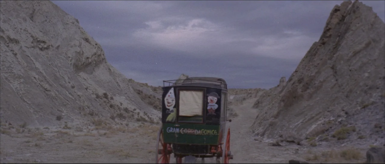 The Mercenary (1968) movie still: wide — A horse-drawn wagon stands on a dirt path between two high, eroded rocky cliffs. The back of the black…