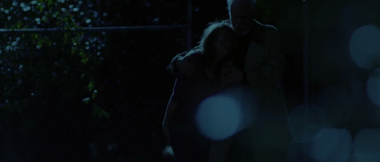 Halloween (2007) movie still: medium — An older man and a younger woman stand before a chain link fence at night. The man has his arm around the…