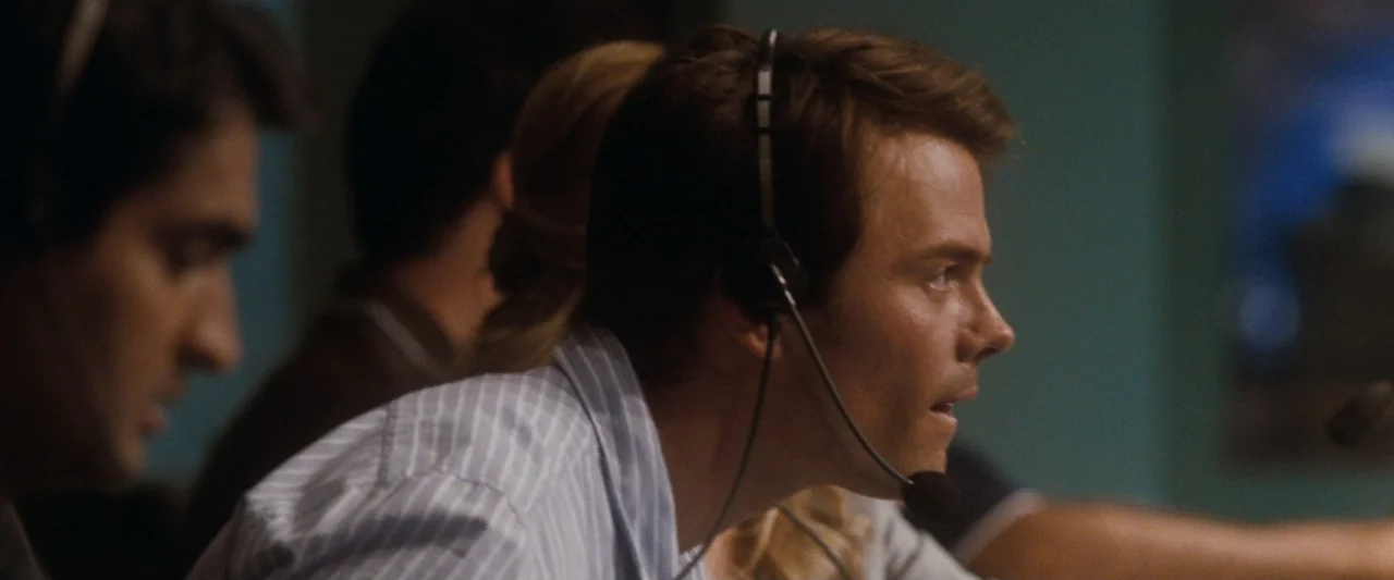 Life As We Know It (2010) movie still: medium — A dimly lit room features personnel seated at workstations with electronic equipment. A man in a…