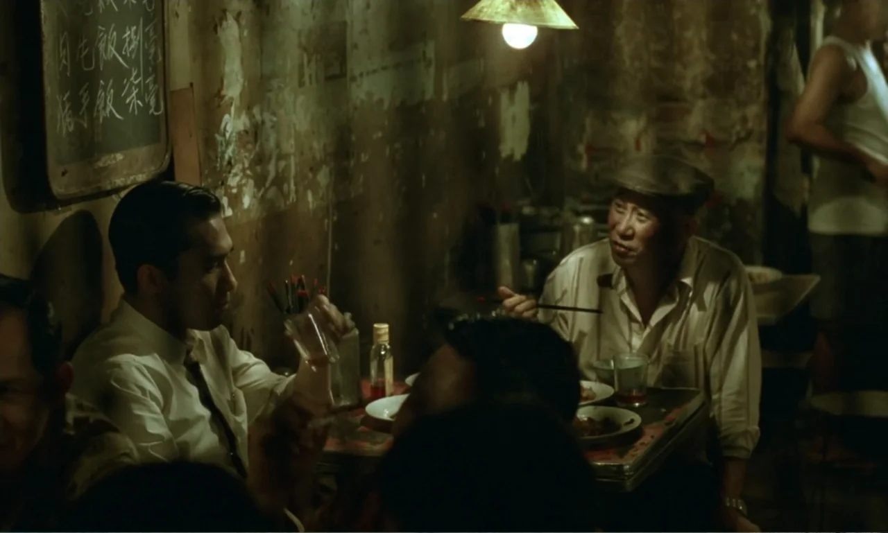 In the Mood for Love (2000) movie still: medium — A cramped, dimly lit establishment features distressed walls with Chinese characters written on a…