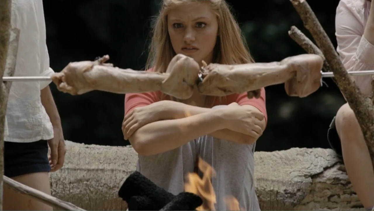 Tomorrow, When the War Began (2010) movie still: medium — A campfire outdoors at night with meat rotating on a metal spit. A young blonde woman…