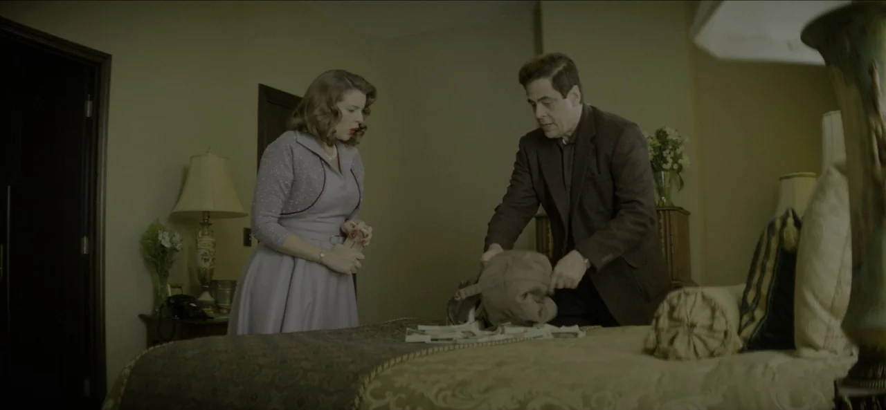 No Sudden Move (2021) movie still: medium — A 1950s style hotel room with muted beige walls and period furniture. A man and a woman stand by the bed…