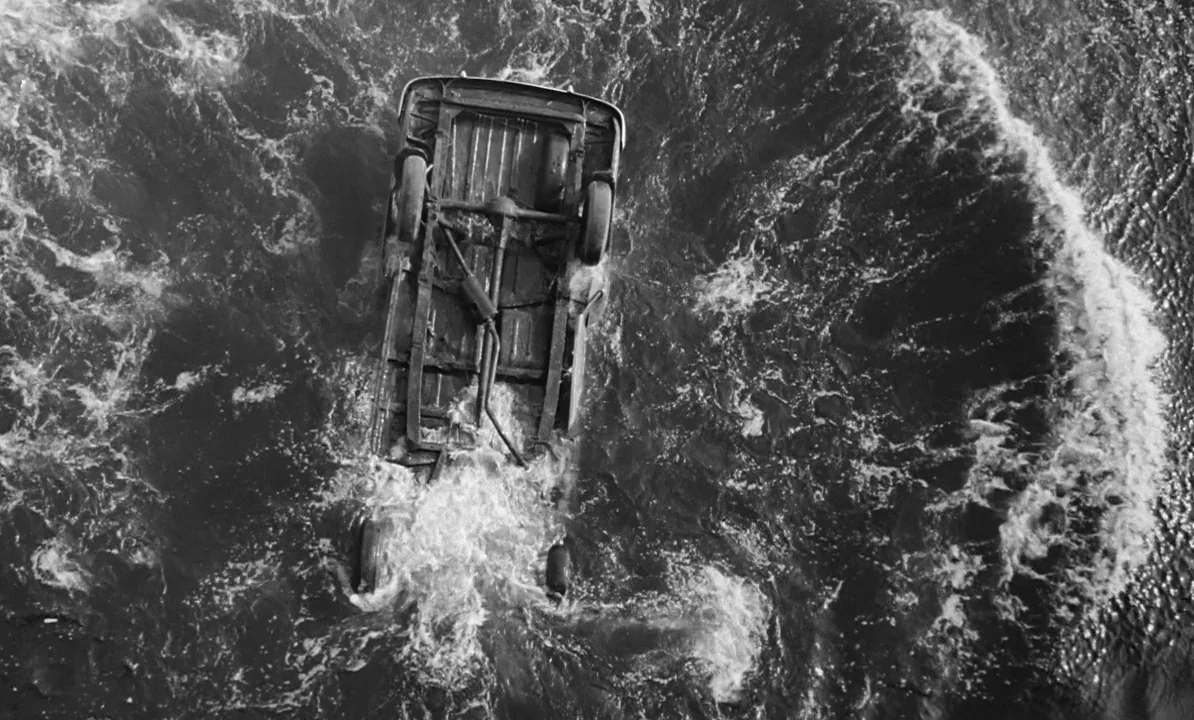 The 1,000 Eyes of Dr. Mabuse (1960) movie still: wide — A vintage car is overturned and floating in the middle of a turbulent river. White foam…