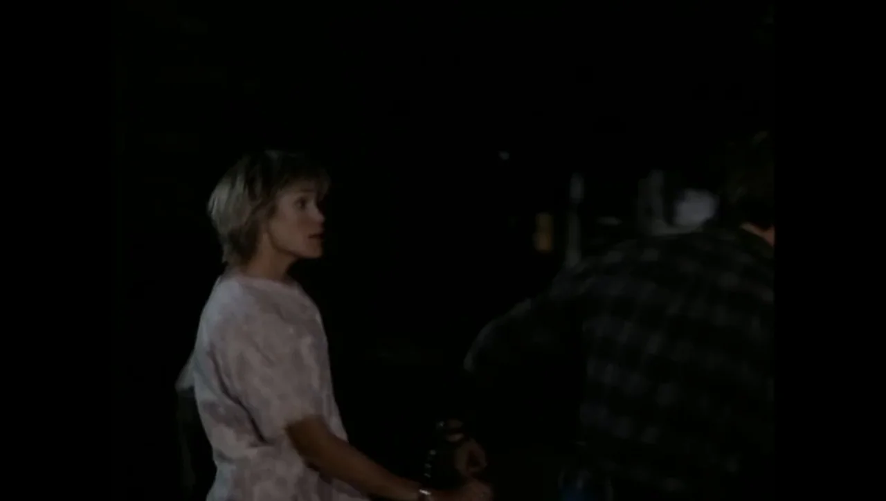 The Awakening (1995) movie still: medium — A dark outdoor setting with minimal detail visible behind the subjects. A young woman turns to look at a…