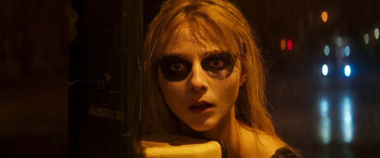 Last Night in Soho (2021) movie still: closeup — A woman stands beside a dark vertical pole on a street at night. She has smeared dark makeup around…