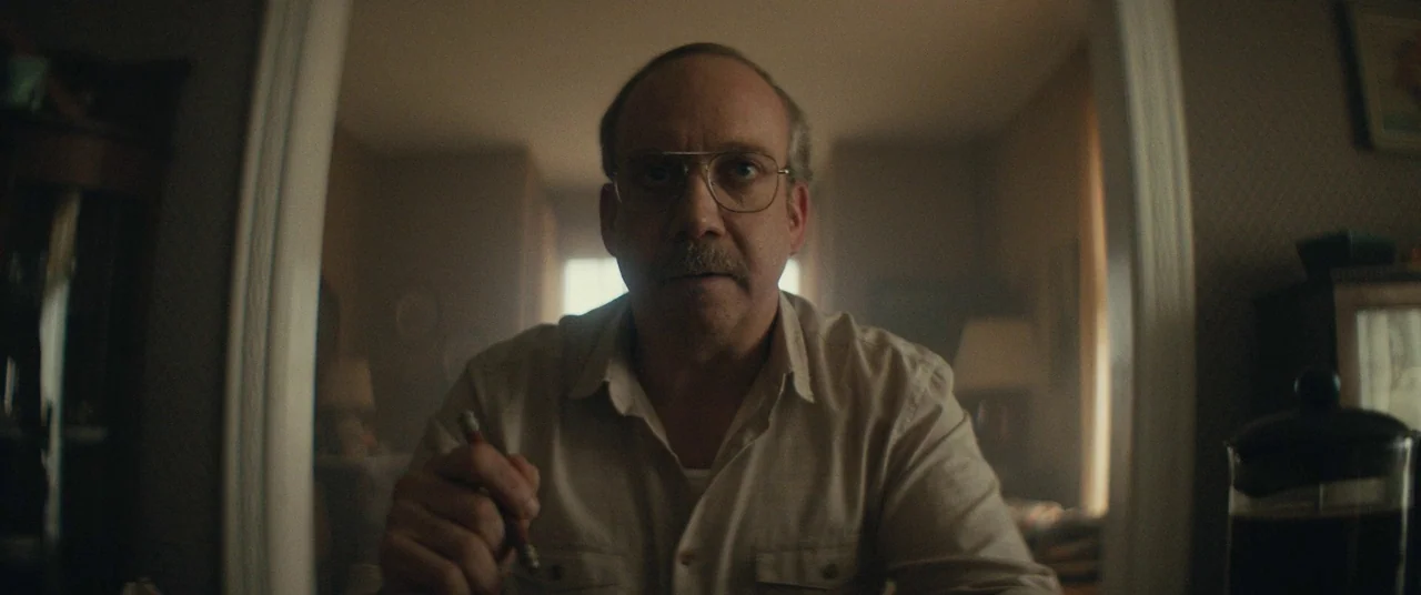 I Think We’re Alone Now (2018) movie still: medium — A dimly lit room with a doorway framing the subject in the background. A man sits at a table…