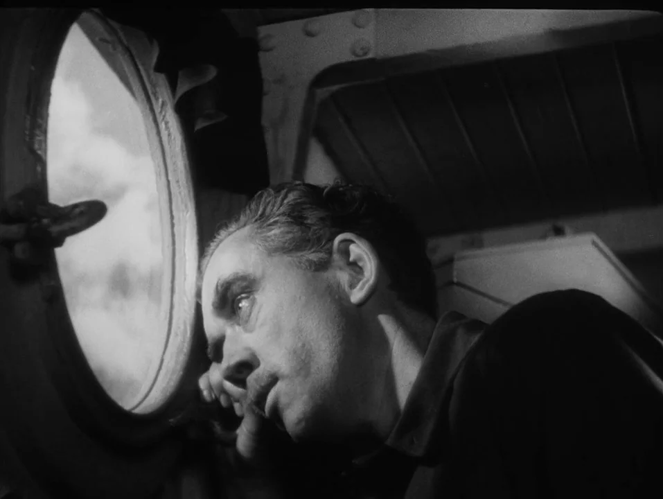 A Ship Bound for India (1947) movie still: closeup — A dark cabin interior features a circular porthole showing a bright, cloudy sky outside. A…