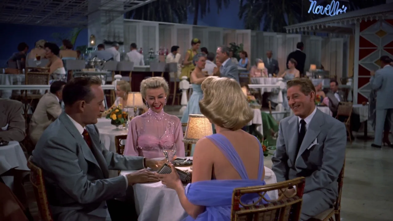 White Christmas (1954) movie still: medium — A crowded mid-century nightclub features white lattice walls and tables with small lamps. Four adults…