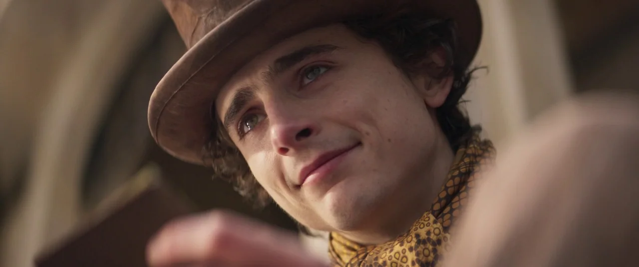Wonka (2023) movie still: closeup — An outdoor setting features a man wearing a brown top hat under natural light. The subject is looking away from…