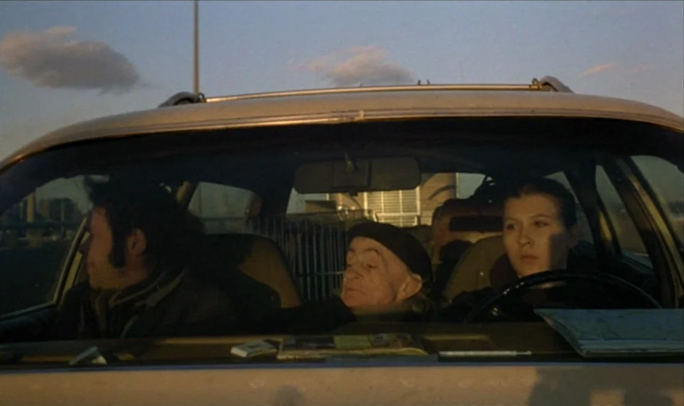 Stroszek (1977) movie still: medium — Three individuals travel in the front seat of a car during the late afternoon. A young woman drives, while an…