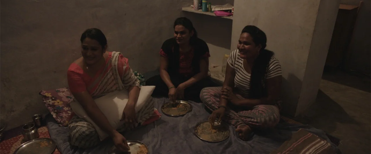 Peranbu (2019) movie still: medium — A sparsely furnished room with concrete walls and floor covered by a cloth mat. Three women sit on the floor…