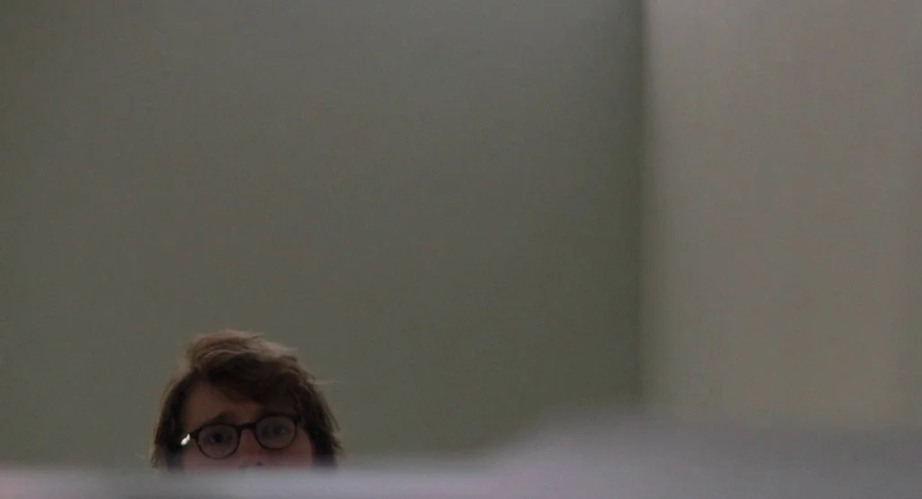 Ruby Sparks (2012) movie still: closeup — A plain, light-colored wall serves as the backdrop in an interior space. A person with brown hair and…