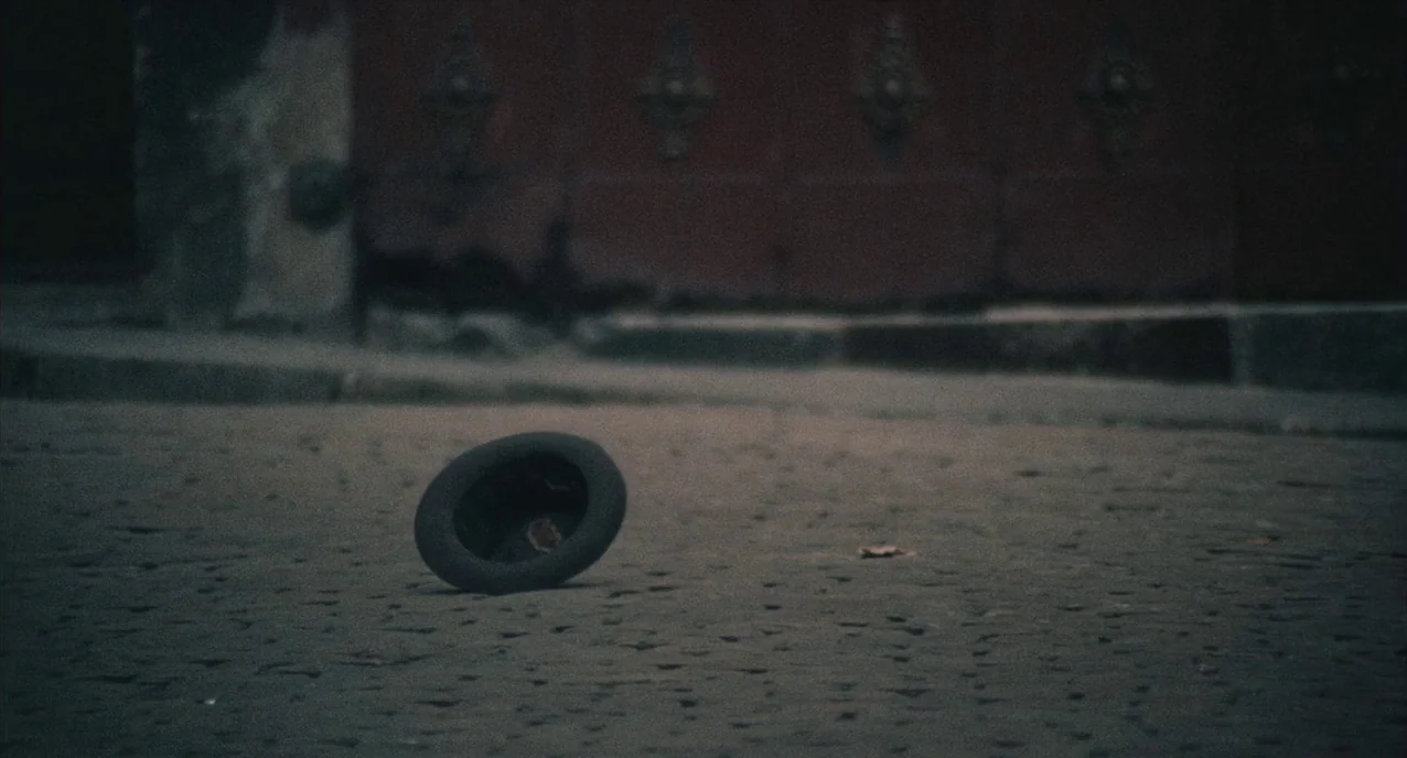 The Army of Shadows (1969) movie still: wide — A dark, empty paved area sits before a large, weathered door with metal accents. A solitary hat lies…