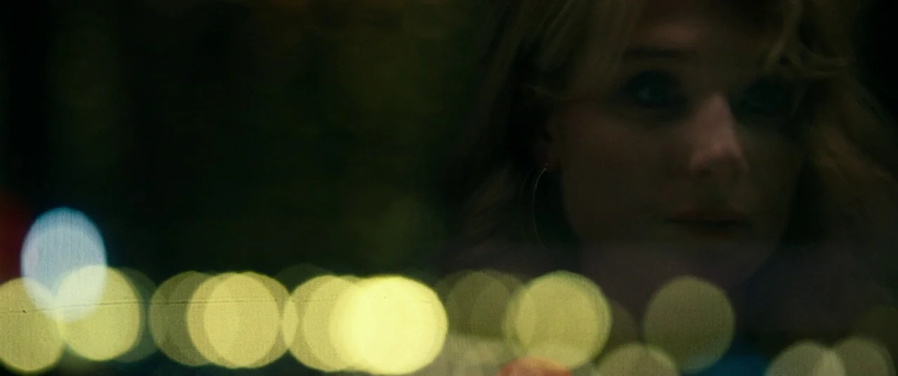 Widows (2018) movie still: closeup — A woman looks out a vehicle window at night with bokeh light reflections. The subject is partially obscured and…