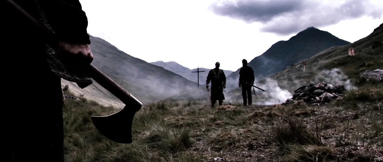 Valhalla Rising (2009) movie still: wide — A desolate, grassy Highland valley features wooden crosses stuck into the uneven earth. Two armed men…
